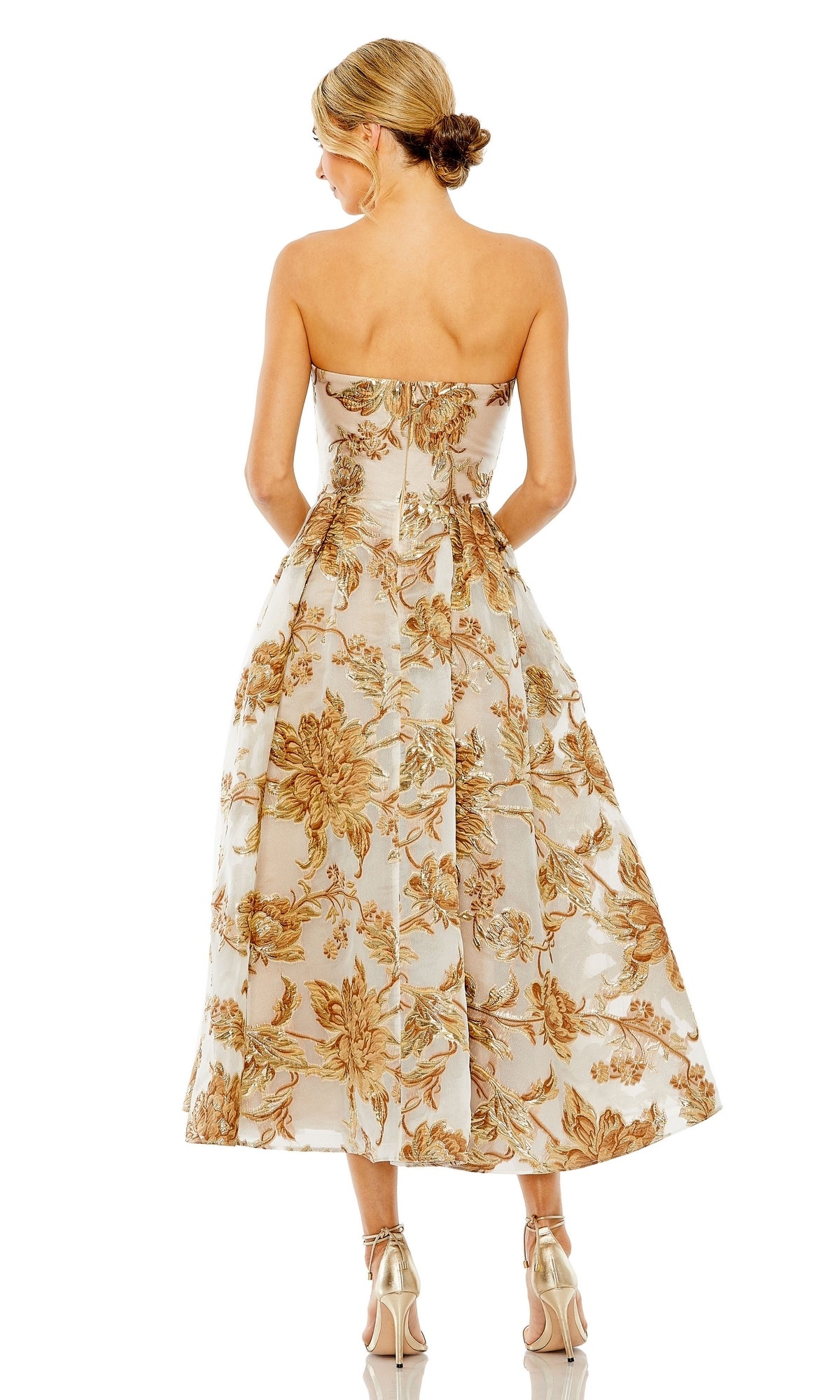 A woman in the Mac Duggal 20716 strapless bronze party dress with a gold floral pattern and metallic heels stands with her back to the camera—a glamorous look for any cocktail event.